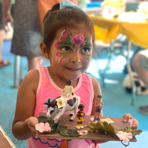 A child in facepaint holds their finished reuse project