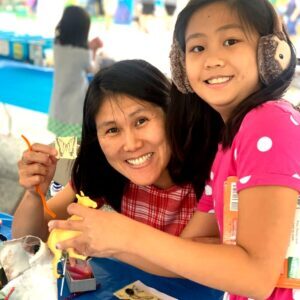 Adult and child smile at the camera as they work on a reuse art project.