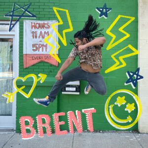 A photo of a person jumping in a karate like pose in front of a green wall with various illustrated doodles added on top.