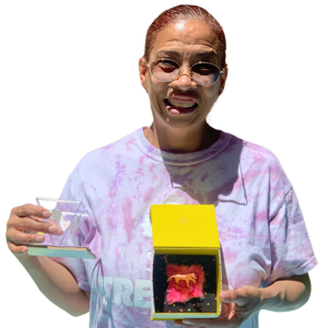 An adult with glasses in a pink shirt shows their finished shadowbox project.